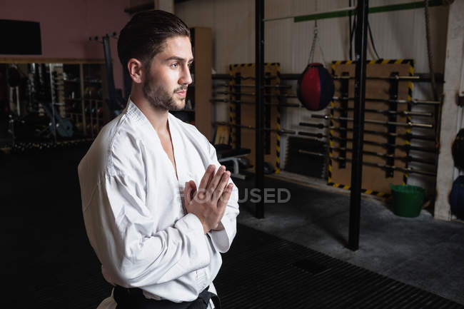 Side view of Man in karate kimono standing with hands in namaste gesture in fitness studio — Stock Photo