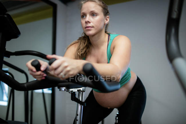 Pregnant woman working out on exercise bike at gym — Stock Photo