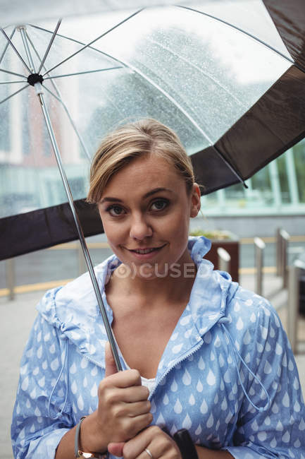 Porträt einer schönen Frau, die während der Regenzeit einen Regenschirm hält und in die Kamera schaut — Stockfoto
