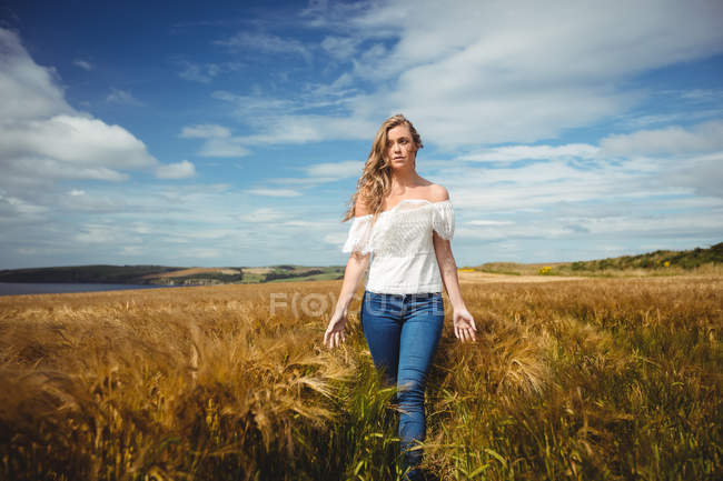Atractiva mujer caminando a través de campo de trigo en día soleado - foto de stock