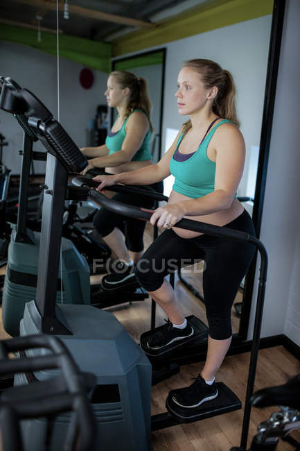 Mujer embarazada haciendo ejercicio en la máquina elíptica en el gimnasio - foto de stock