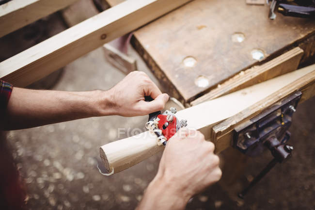 Man using a handheld tool to smooth and level the surface of a plank in boatyard — Stock Photo