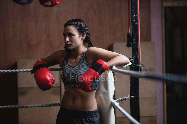 Tired boxer in boxing gloves leaning on ropes of boxing ring at fitness studio — Stock Photo