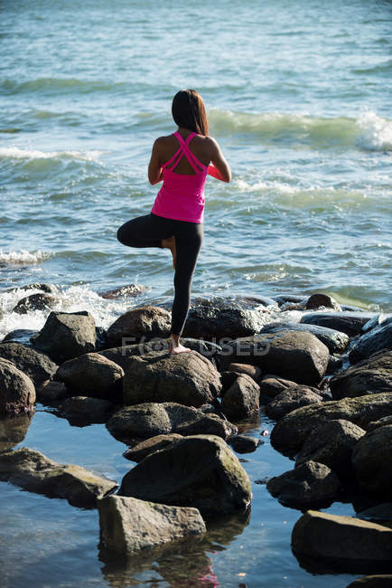 Vista trasera de la mujer realizando yoga sobre rocas en un día soleado - foto de stock