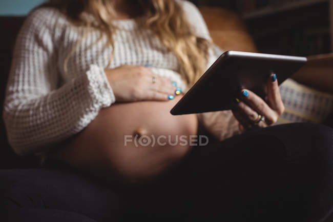 Обрезанный образ беременной женщины с помощью цифрового планшета в гостиной на дому — стоковое фото