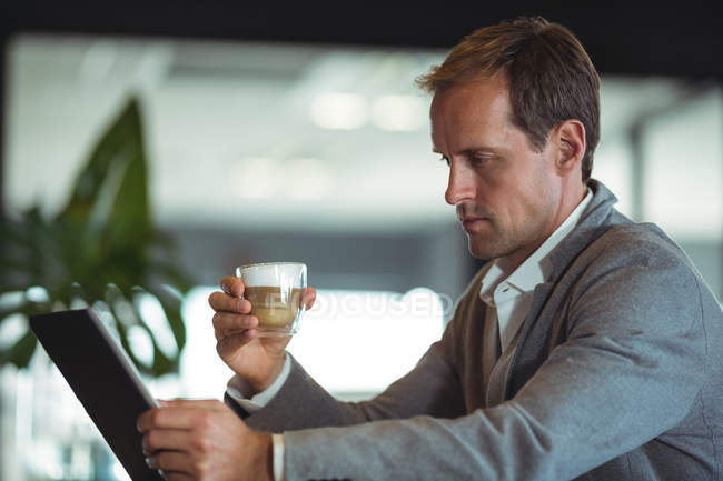 Empresario tomando café mientras trabaja en tableta digital en la cafetería - foto de stock