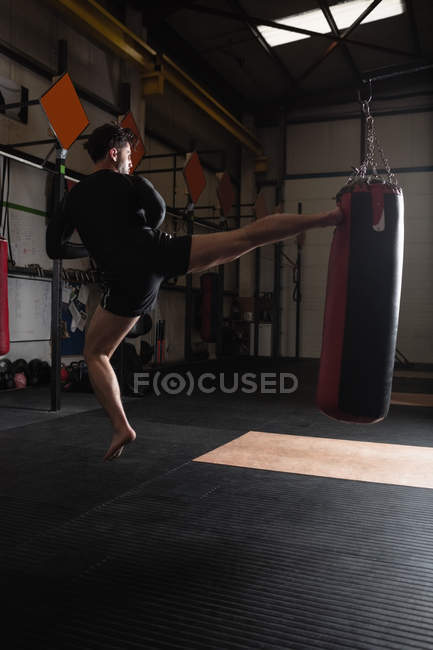 Vista trasera del boxeador masculino practicando boxeo con saco de boxeo en gimnasio - foto de stock