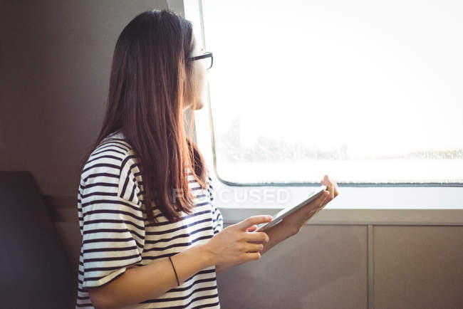 Jovem mulher olhando através da janela ao usar tablet digital — Fotografia de Stock