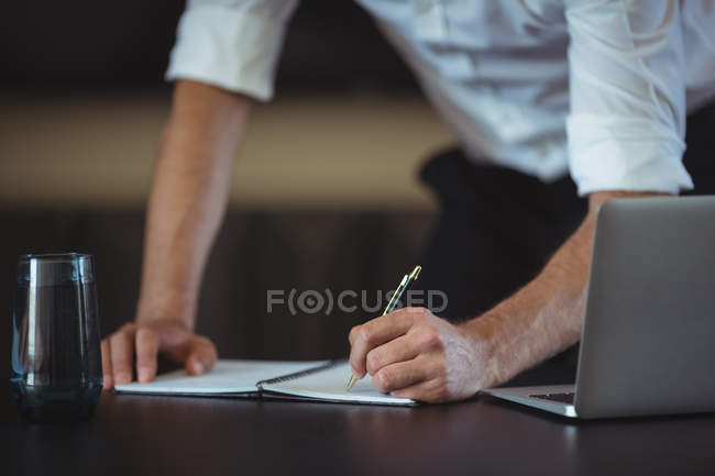 Бизнесмен пишет в блокноте на столе в офисе — стоковое фото
