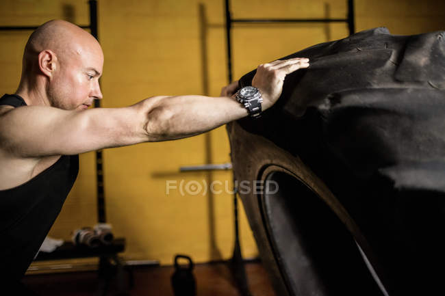 Handsome sportsman lifting heavy tire in gym — Stock Photo
