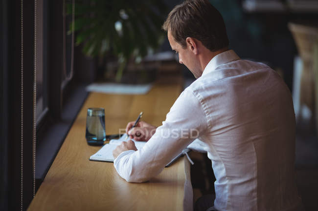 Empresário escrevendo em diário na mesa no escritório — Fotografia de Stock