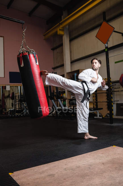 Человек, практикующий карате с боксерской грушей в фитнес-студии — стоковое фото