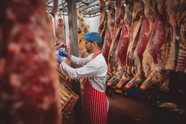 Açougueiro pendurado carcaças de carne vermelha na sala de armazenamento no açougue — Fotografia de Stock