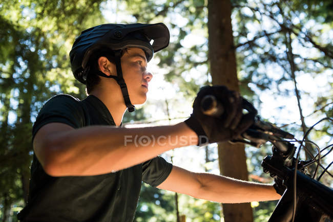 Ciclista masculino caminhando com mountain bike na floresta — Fotografia de Stock