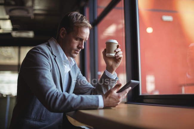 Бизнесмен, пользующийся мобильным телефоном за чашечкой кофе в кафе — стоковое фото