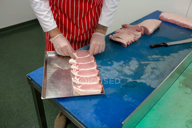 Mid section of butcher arranging steaks in tray at butchers shop — Stock Photo