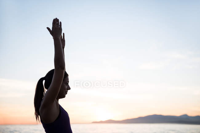 Vista lateral de la mujer practicando yoga en la playa al atardecer - foto de stock