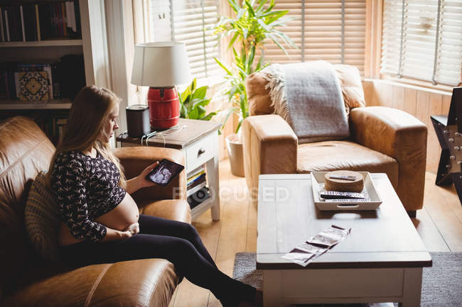 Вагітна жінка дивиться на зображення сонографії на планшеті у вітальні — стокове фото