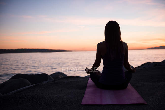 Вид ззаду жінки, що практикує йогу на пляжі в сутінках — стокове фото