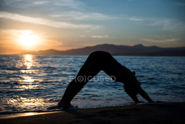 Вид сбоку на женщину, занимающуюся йогой на пляже во время заката — стоковое фото