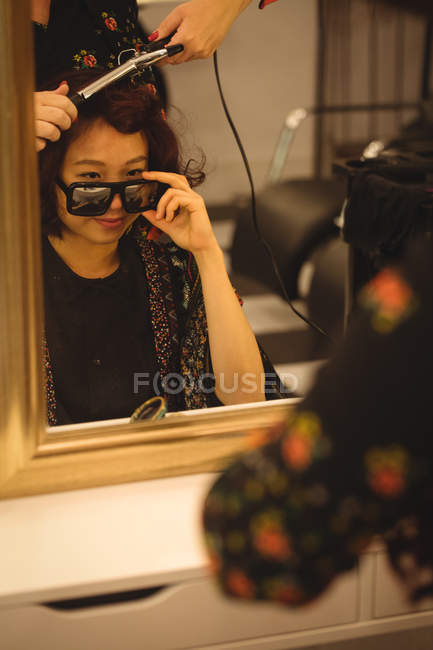 Stylish woman looking over sunglasses while getting her hair done at a professional hair salon — Stock Photo