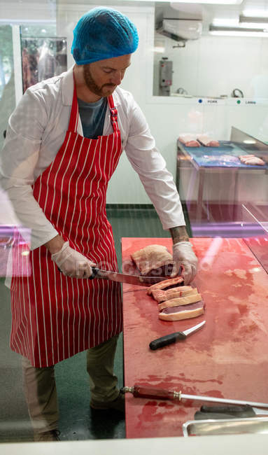 Carnicero rebanando carne en la carnicería - foto de stock