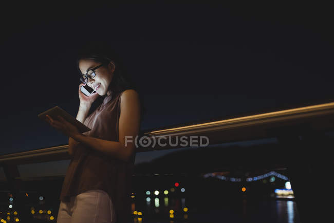 Молода жінка розмовляє на мобільному телефоні, використовуючи цифровий планшет — стокове фото