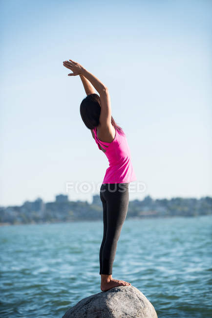 Вид збоку жінки, що виконує йогу на скелі в сонячний день — стокове фото