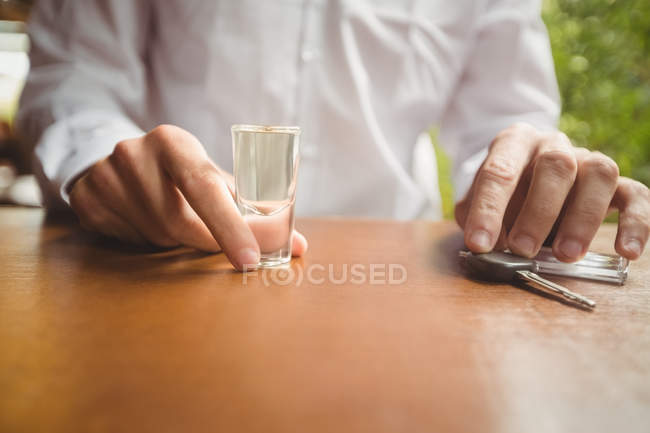Seção média do homem segurando vidro de tequila tiro e chave do carro no balcão de bar no bar — Fotografia de Stock