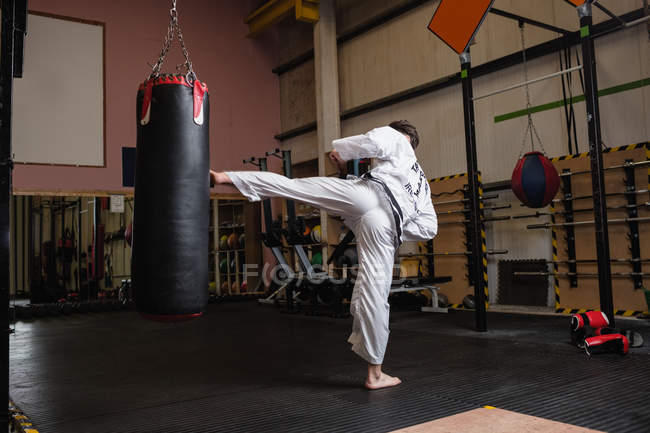 Visão traseira do homem praticando karatê com saco de perfuração no estúdio de fitness — Fotografia de Stock