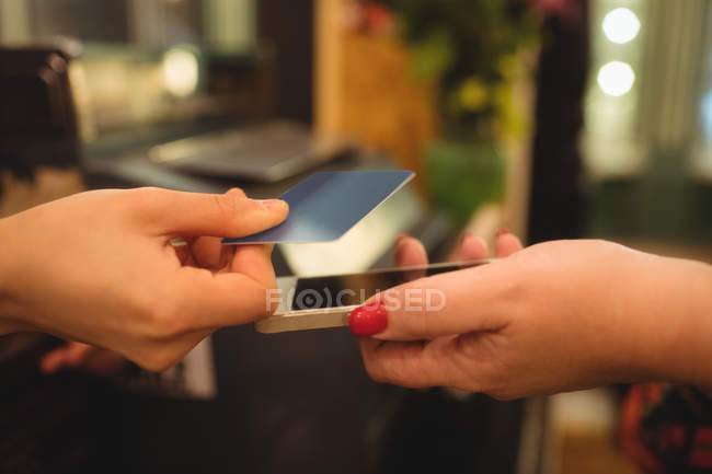 Cliente dando telefone e cartão de crédito para caixa no balcão de faturamento — Fotografia de Stock