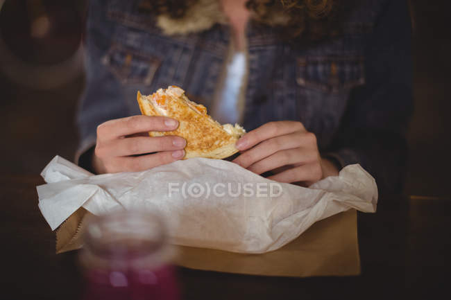 Средняя часть женщины, сидящей за столом и поедающей сэндвичи в магазине велосипедов — стоковое фото