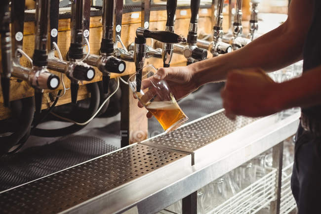 Mid section of bar tender filling beer from bar pump at bar counter — Stock Photo