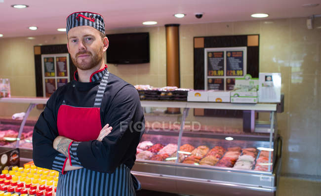 Boucher debout dans un magasin de viande avec les bras croisés — Photo de stock
