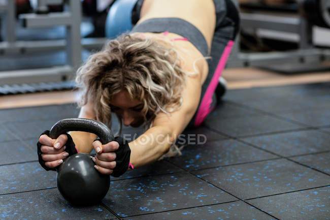 Woman performing stretching exercise with kettlebell in gym — Stock Photo