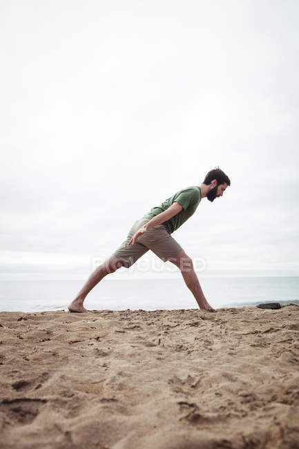 Hombre realizando ejercicio de estiramiento en la playa - foto de stock