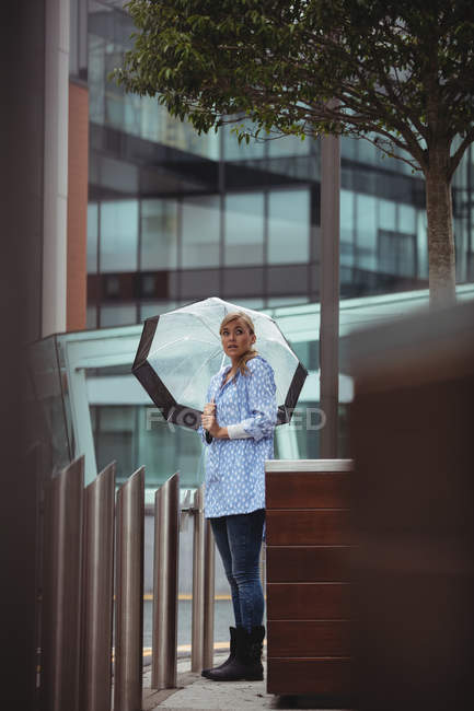 Hermosa mujer sosteniendo paraguas y de pie en la calle durante la temporada de lluvias - foto de stock