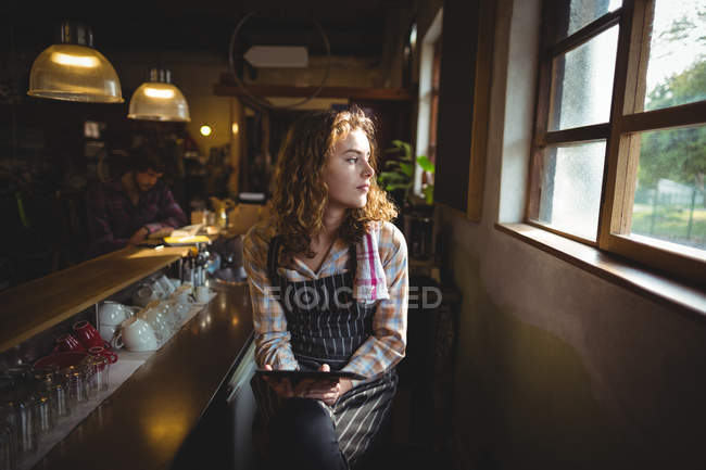 Задумчивая официантка сидит за прилавком и смотрит в окно в мастерской — стоковое фото