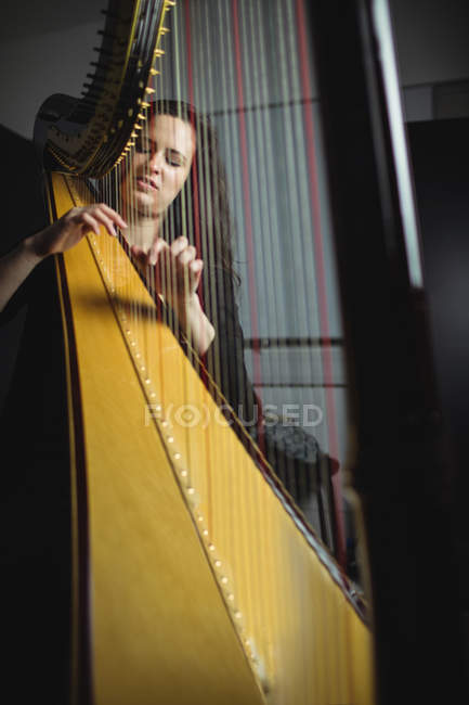 Mujer atenta tocando un arpa en la escuela de música - foto de stock