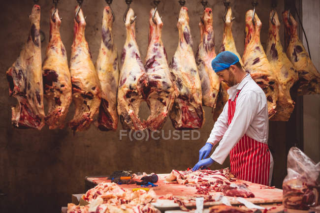 Мясник режет мясо на складе мясной лавки. — стоковое фото