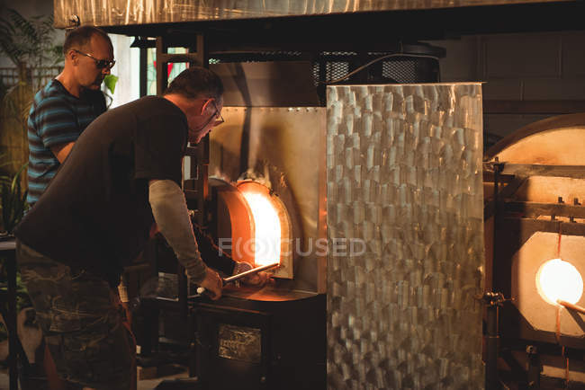 Squadra di soffiatori riscaldamento vetro in forno presso la fabbrica di soffiaggio vetro — Foto stock