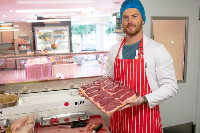 Carnicero sosteniendo una bandeja de filetes en la carnicería - foto de stock