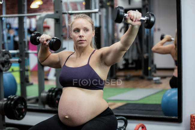 Pregnant woman lifting dumbbells at gym — Stock Photo
