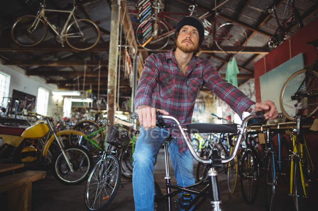 Pensativo mecánico sentado en bicicleta en la tienda de bicicletas - foto de stock