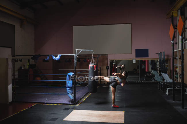 Visão traseira do boxer feminino chutando saco de perfuração no estúdio de fitness — Fotografia de Stock