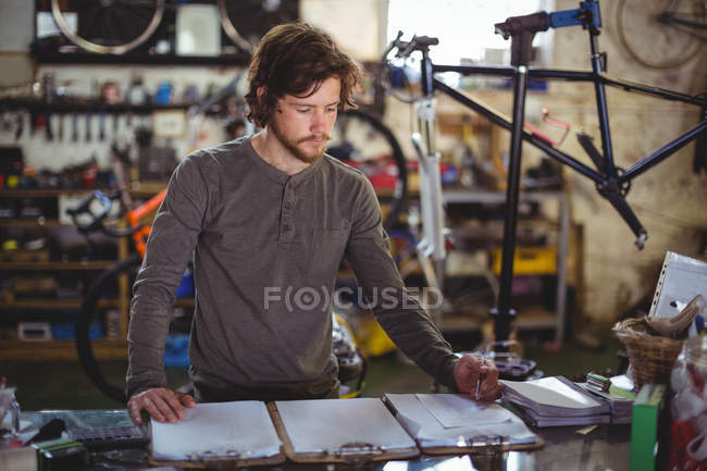 Mechanic writing on clipboard at counter in bicycle shop — Stock Photo