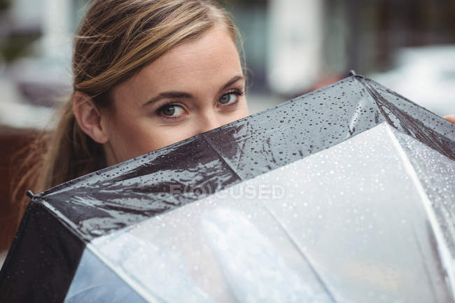 Beautiful woman covering her face with umbrella during rainy season — Stock Photo