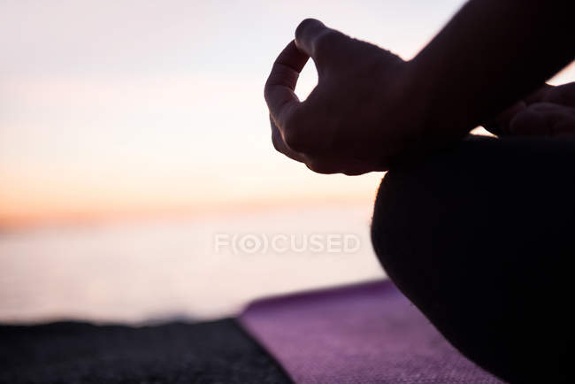 Imagem cortada de mulher sentada em posição de lótus com gesto mudra na praia ao entardecer — Fotografia de Stock
