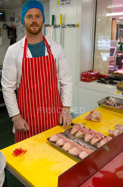 Carniceiro macho de pé com bandeja de rolos de frango e bife — Fotografia de Stock