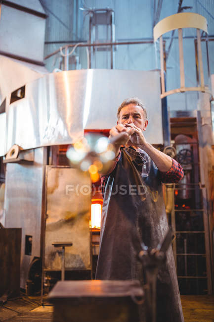 Soffiatore di vetro che modella un vetro sul blowpipe alla fabbrica di soffiaggio del vetro — Foto stock